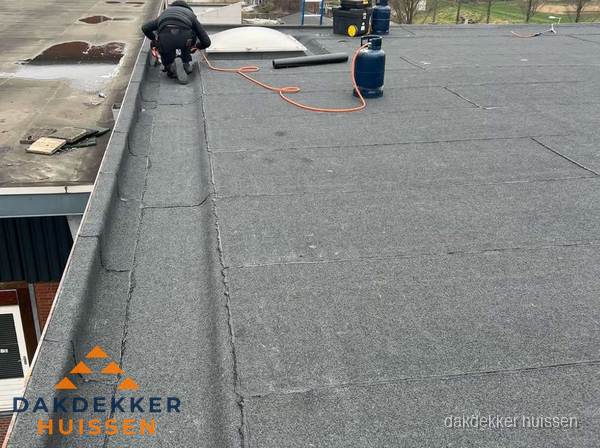 Dakdekker repareert bitumen dakbedekking op groot plat dak in Huissen